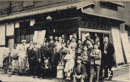 old sepia-toned photo of a group of people standing in front of a building