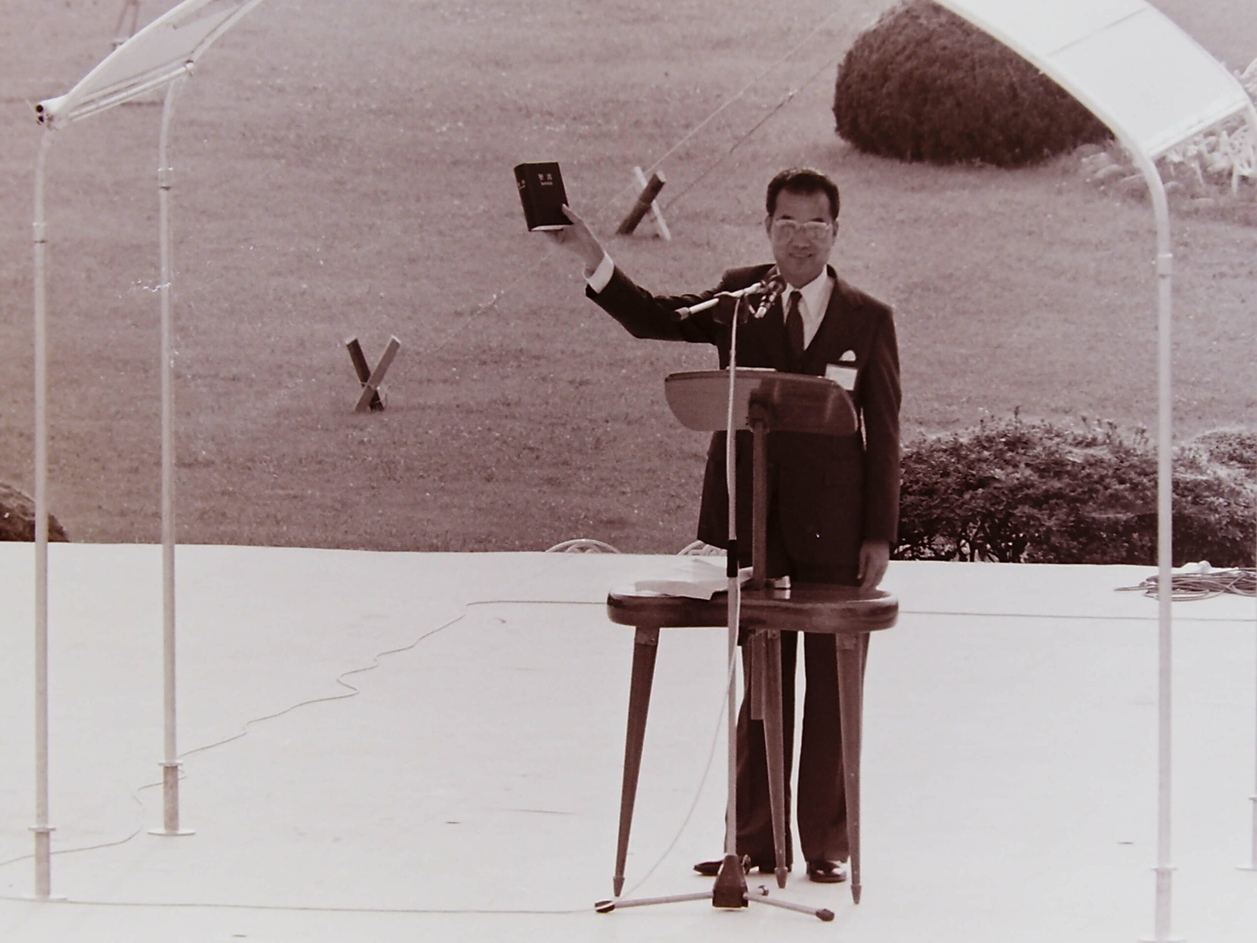 an old photo with a man standing behind a lectern holding a Bible in a hand raised in the air